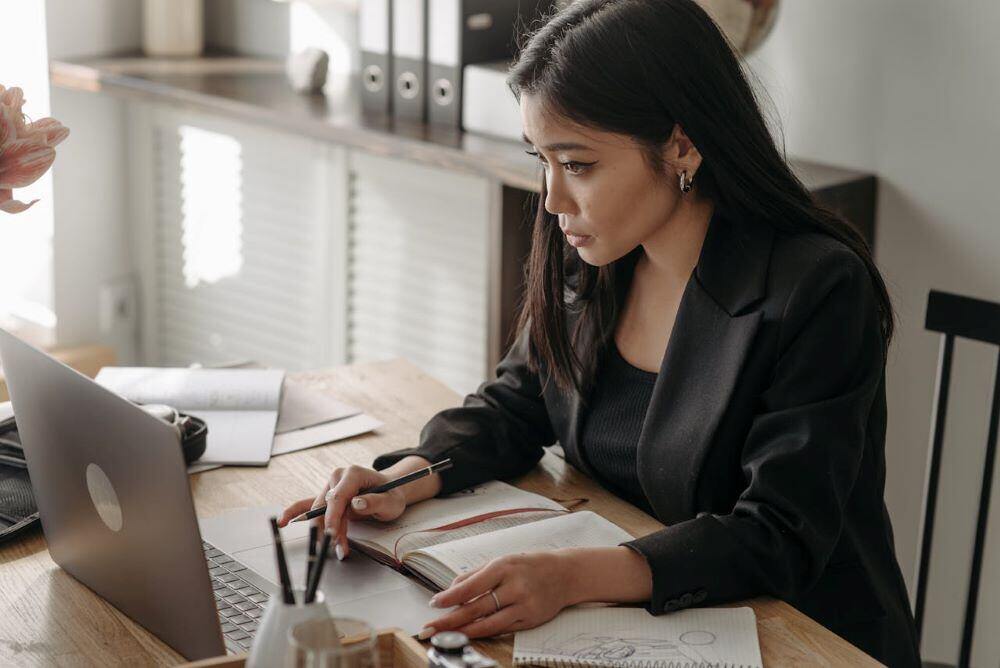 woman taking notes while taking an online course on her laptop