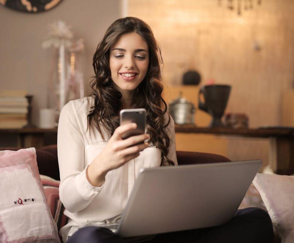 This young woman looking at her phone with her laptop open is one of many Gen Z entrepreneurs whose success is supported by her association