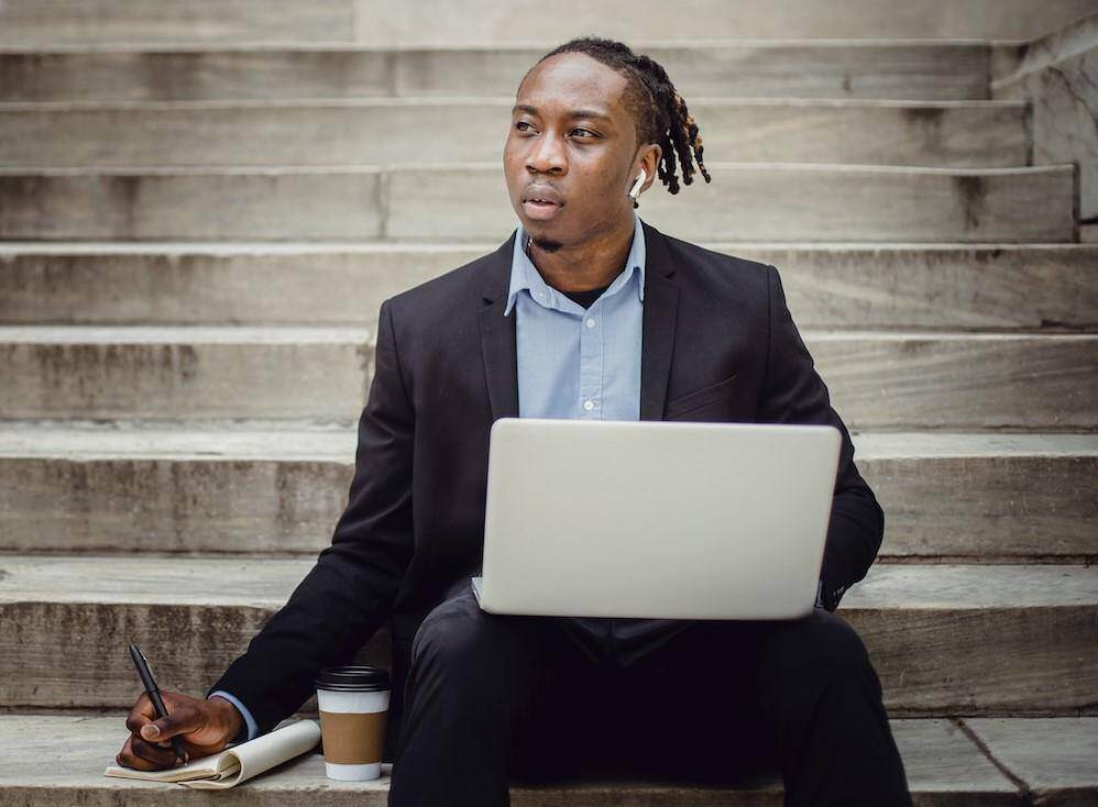 young man sitting on steps with his laptop and developing his professional learning plan