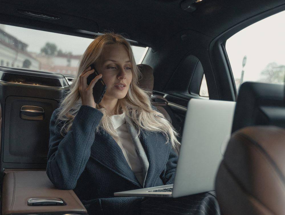 management training program graduate sitting in a town car on her phone and laptop